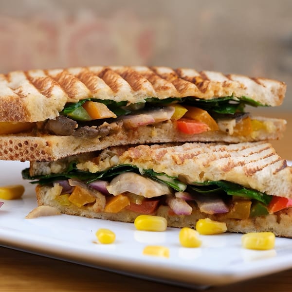 Grilled vegan panini with spinach, mushrooms, bell peppers, and onions, served on a white plate.