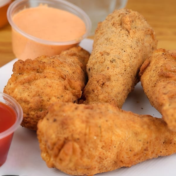 Crispy vegan fried chicken pieces on a white plate with two dipping sauces.