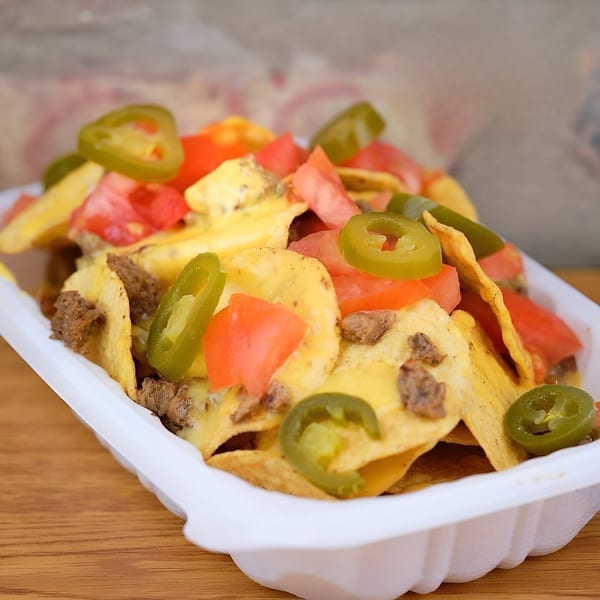 Vegan nachos with cheese sauce, diced tomatoes, vegan ground meat, and jalapeños in a white container.