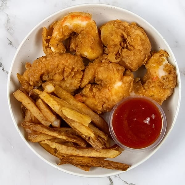 A plate of golden-brown vegan fried shrimp and french fries with a side of red dipping sauce.