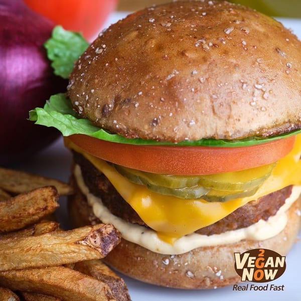 Vegan Now 2 Go vegan burger with cheese, pickles, tomato, lettuce, and a side of fries.