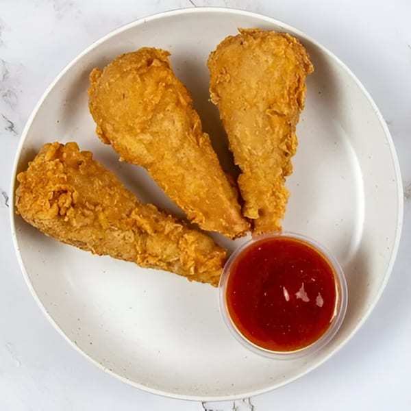 Three golden-brown vegan drumsticks with a side of red dipping sauce on a white plate.
