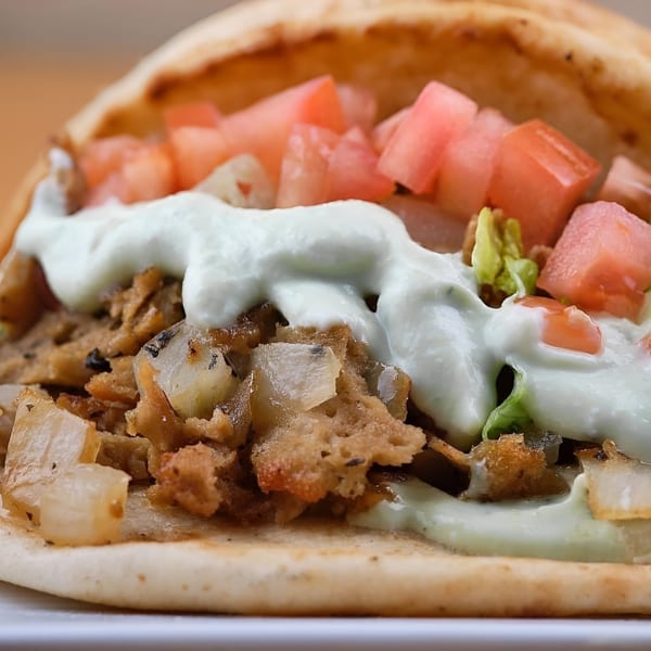 Close-up of a vegan gyro with plant-based meat, diced tomatoes, onions, and white sauce in pita bread.
